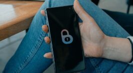 Hånd holder en smarttelefon med et ulåst hengelåsikon på skjermen