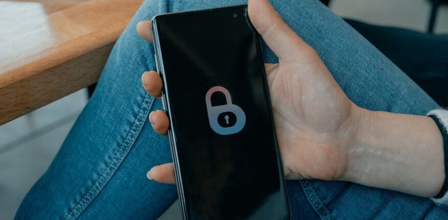 Hånd holder en smarttelefon med et ulåst hengelåsikon på skjermen